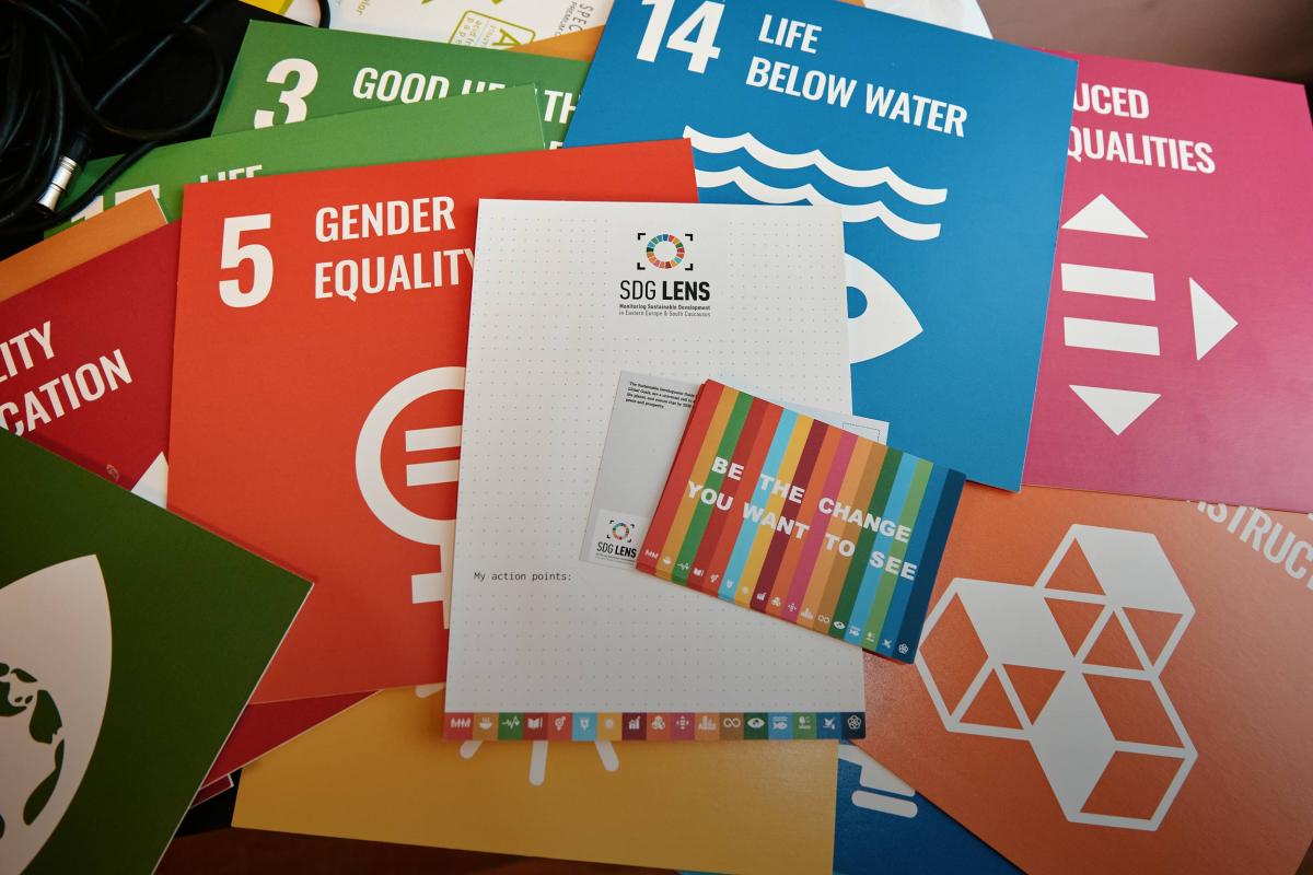 A booklet on the table, in SDG colors, the text on the cover: "Be the change you want to see". Everything is in SDG Lens brand colors.