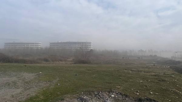 Two buildings standing in light fog, a wasteland in the foreground.