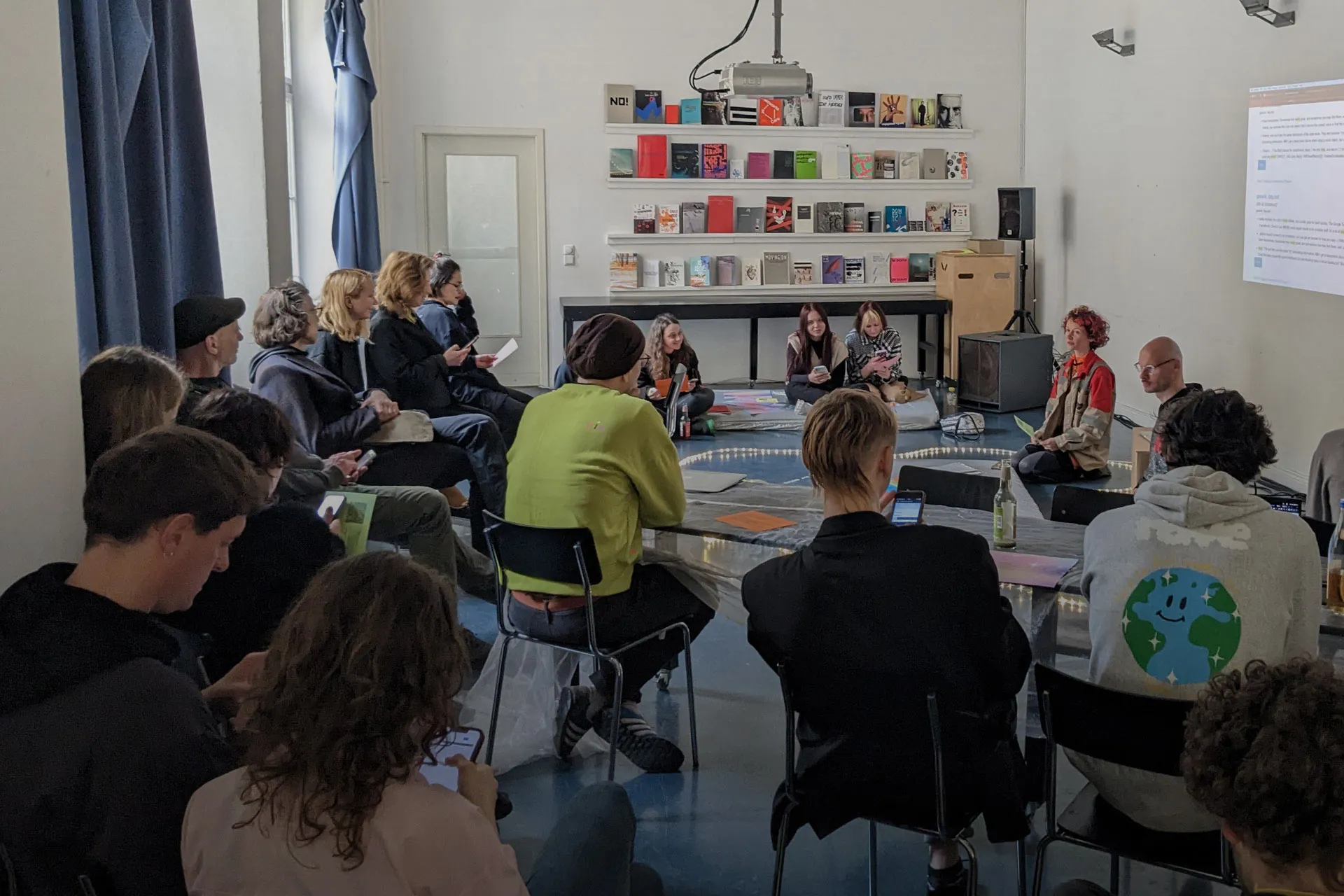 People are sitting in a seminar: two persons are sitting in front of a group of many people.